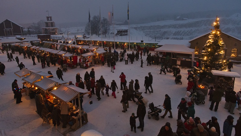 Ett torg i skymning och julmarknad och gnistrande julgransljus.