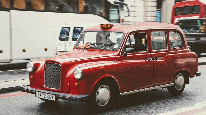 Rd gammeldags taxi bil p gata i London. Fraren sitter till vnster i bilen. 